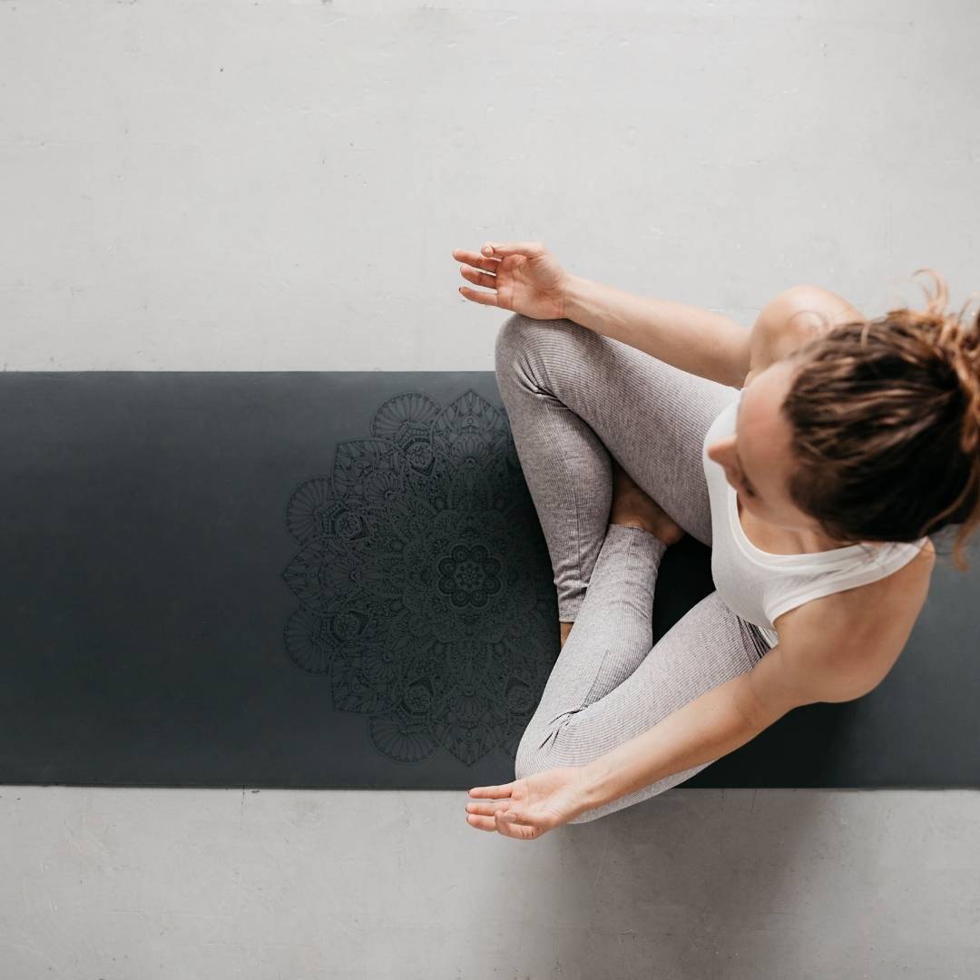 woman in lotus pose on a dark grey yoga mat with a mandala design on it